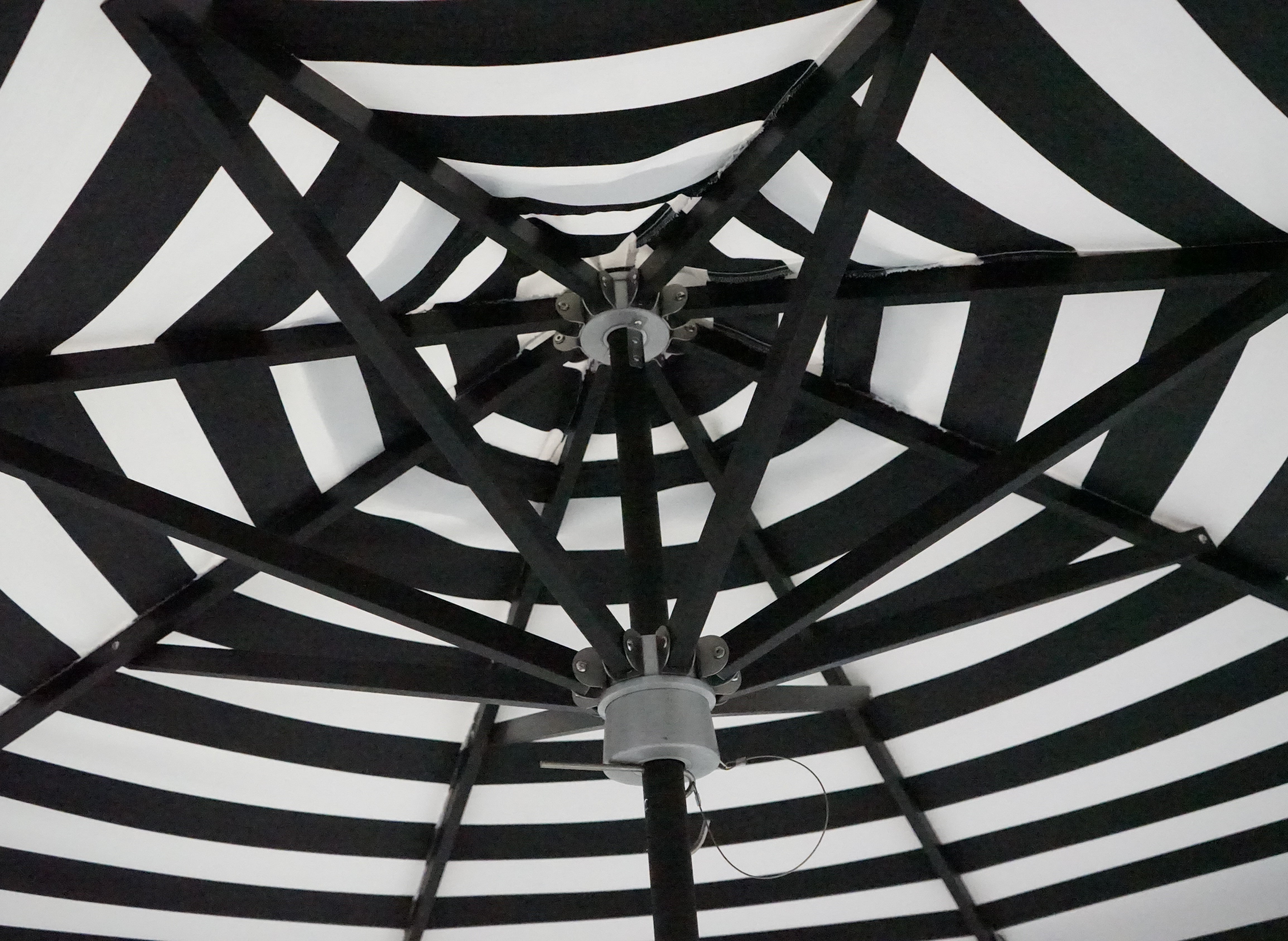 Close-up of a black and white striped umbrella. This image shows the detail of the underside of the umbrella. It has a black frame and aluminum hub. 