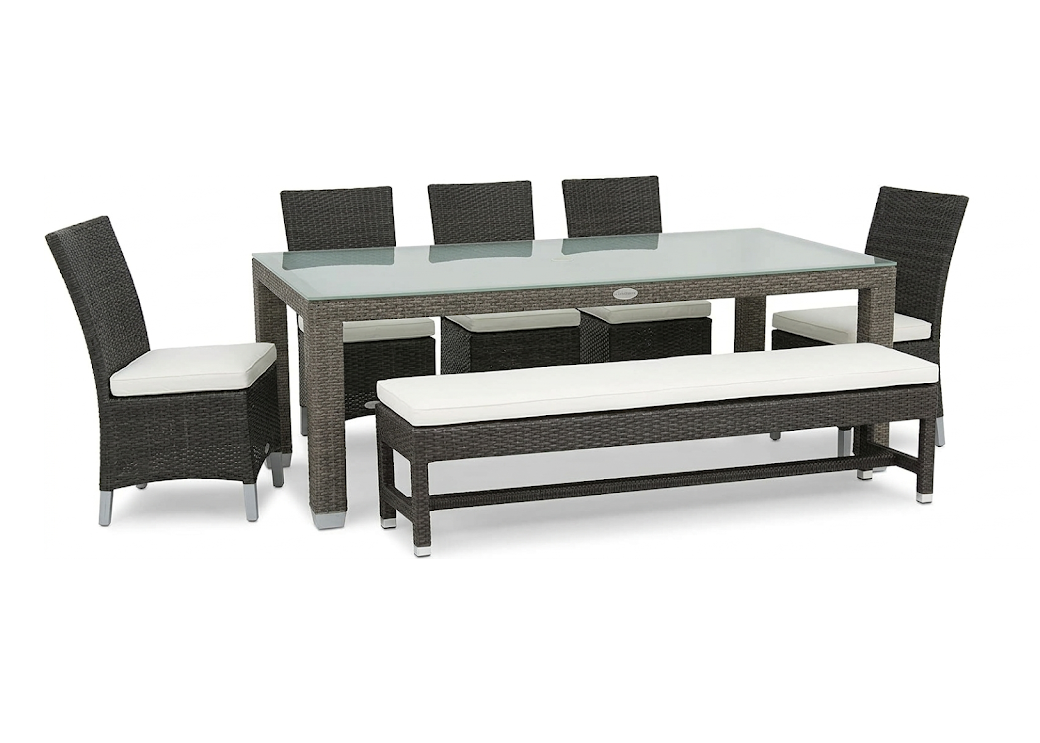 Outdoor dining set with a rectangular table and five dining arm chairs and a bench on a white background. The patio set is a dark brown wicker color with a frosted glass top. The dining chairs have a high solid back with no arms and white seat cushions on them. The bench is at one end of the table which also has one large seat cushion. 